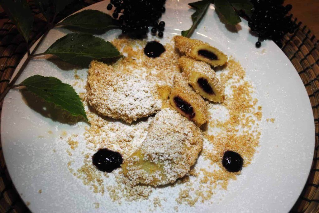 Eachtlingtascherl mit Hollermarmelade, Puderzucker und Beeren auf weißem Teller.