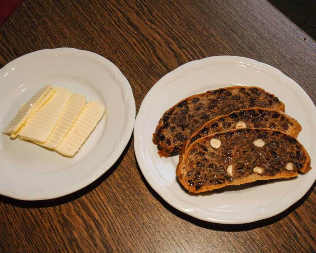 Kletzenbrot-Scheiben mit Butter auf zwei Tellern, serviert auf einem Holzuntergrund.