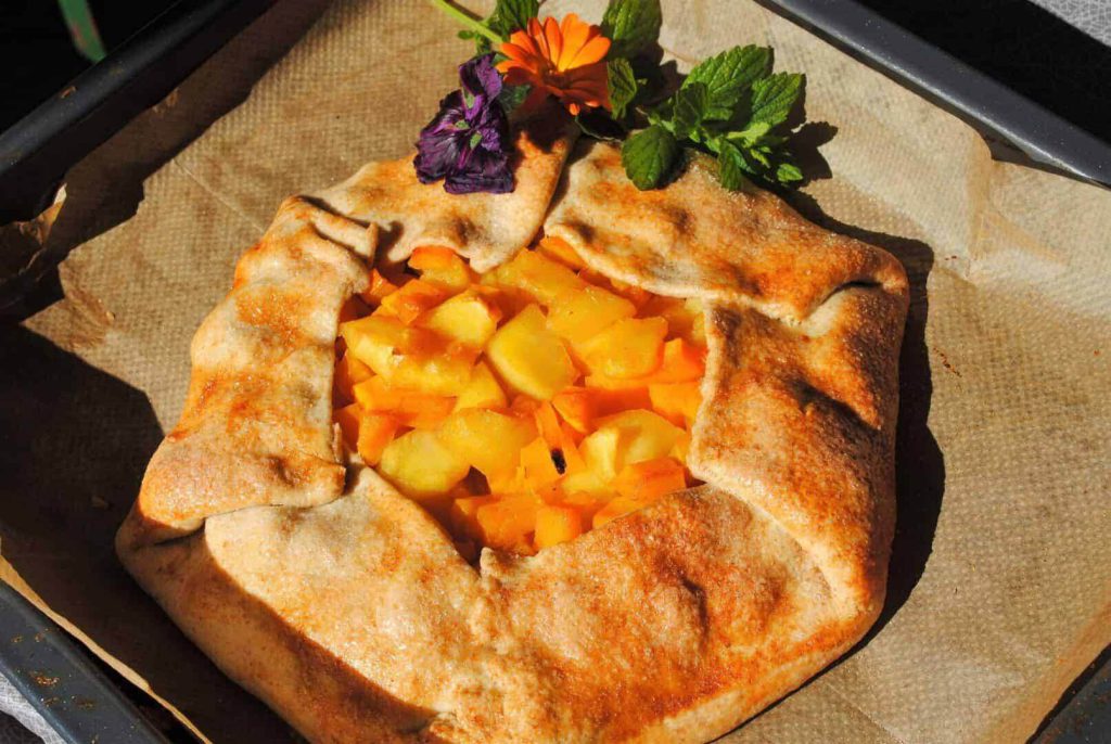 Herzhafte Kürbis-Apfel-Tarte auf Backpapier mit frischen Kräutern dekoriert.