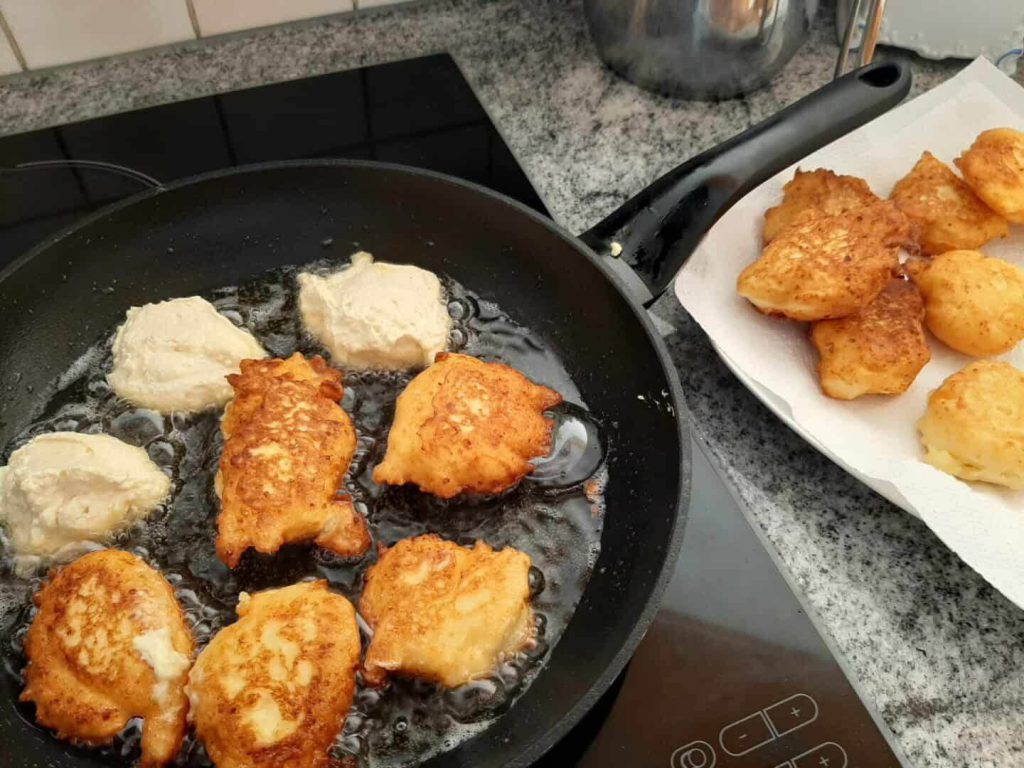 Goldbraun gebratene Topfennudala in einer Pfanne, daneben fertig gebratene Stücke.