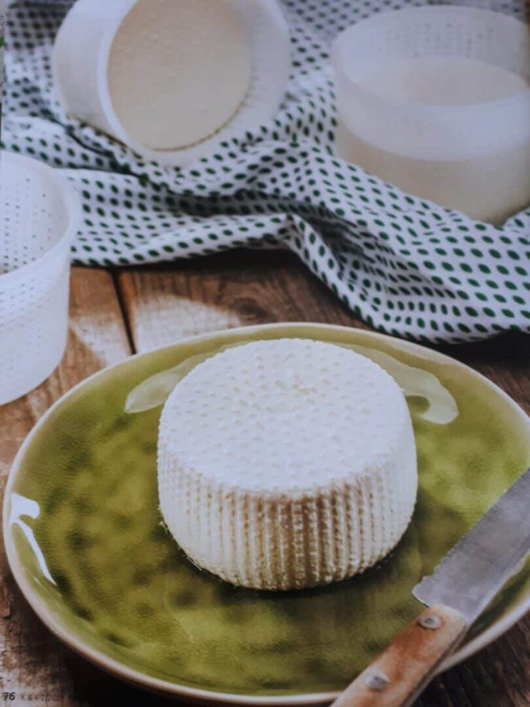Weichkäse auf grünem Teller, umgeben von Käseformen und einem Messer.