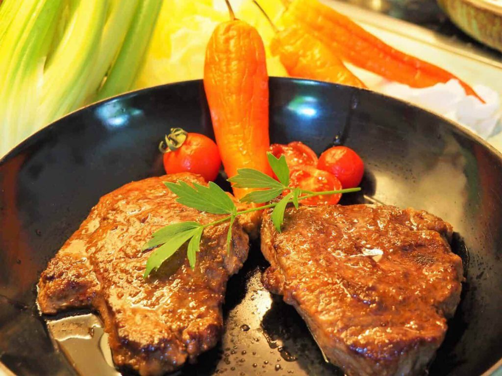 Gebratenes Hüftsteak mit frischem Gemüse und Kräutern auf einem schwarzen Teller.