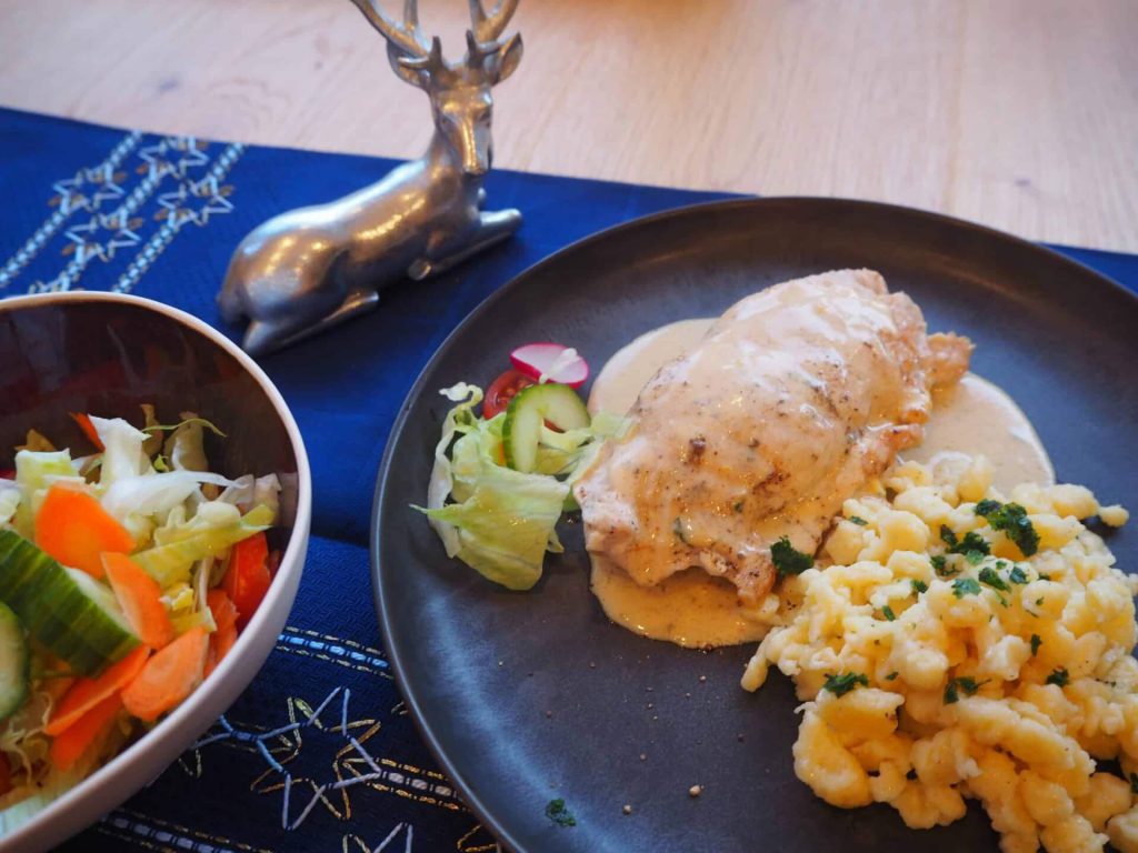 Lungauer Schnitzel in Sahnesoße mit Spätzle und frischem Salat auf dunklem Teller.